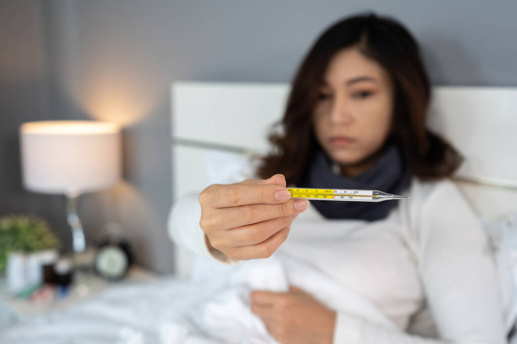 хвора жінка використовує термометр і показує високу температуру в ліжку
 - Фото, зображення