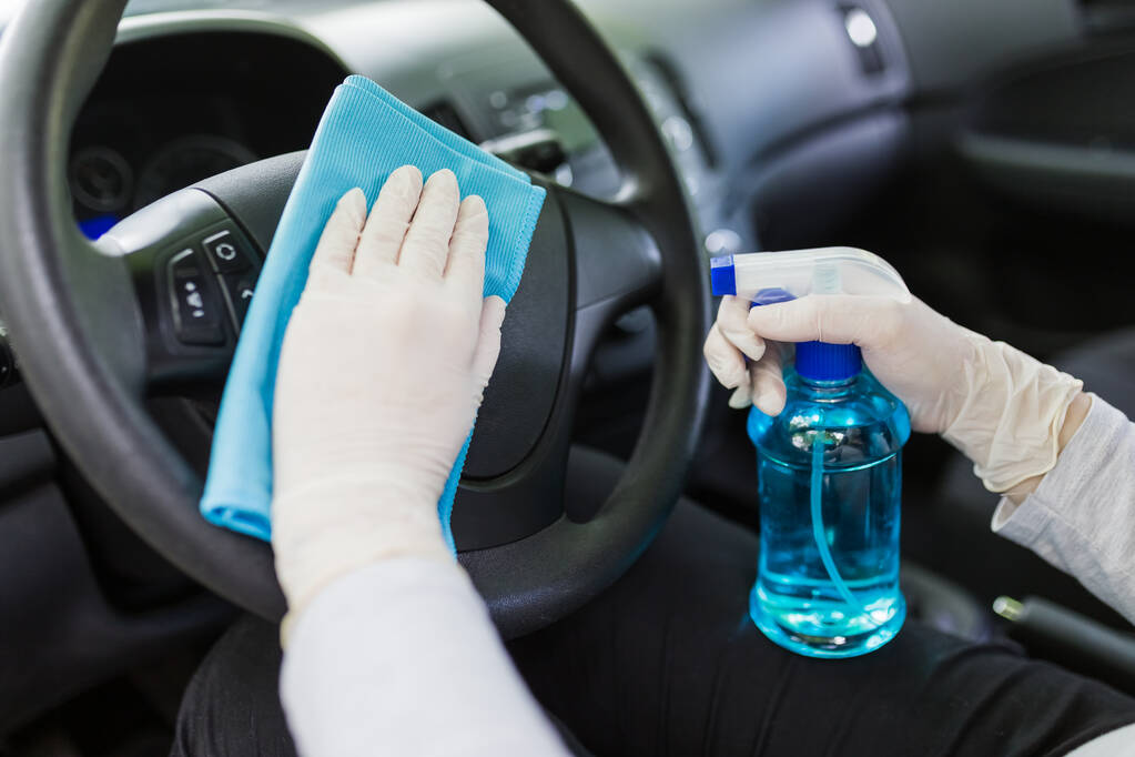 Travailleur féminin nettoyage volant de voiture avec chiffon en microfibre et tenant vaporisateur de désinfectant
. - Photo, image