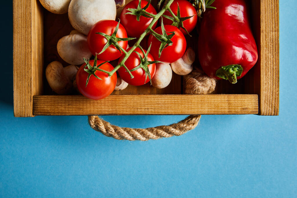 top view of mushrooms near red cherry tomatoes and chili pepper in wooden box on blue - Photo, Image
