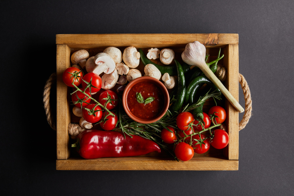 vue de dessus de la sauce tomate avec des feuilles de basilic près de tomates cerises, piments verts, champignons et romarin dans une boîte en bois sur noir
 - Photo, image