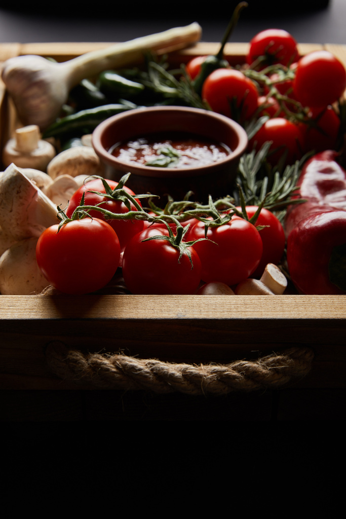 selektivní zaměření hub, červených cherry rajčat, rajčatové omáčky v blízkosti rozmarýnu a chilli papriček v dřevěné krabici  - Fotografie, Obrázek