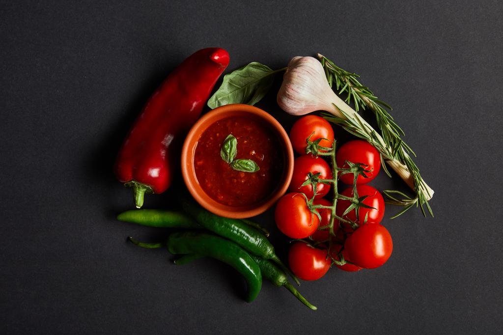 vista superior de tomates cereja maduros, alho, molho de tomate em tigela e alecrim perto de pimentas em preto
 - Foto, Imagem