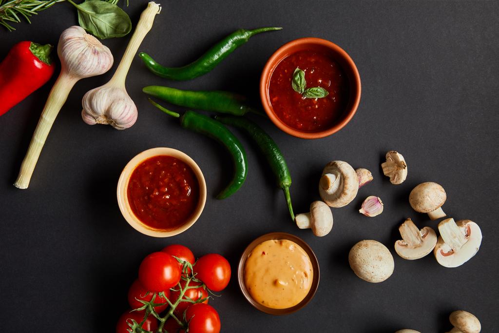 Olgun sebzelerin yanında kırmızı domates ve hardal soslu siyah kaselerin üst görüntüsü. - Fotoğraf, Görsel