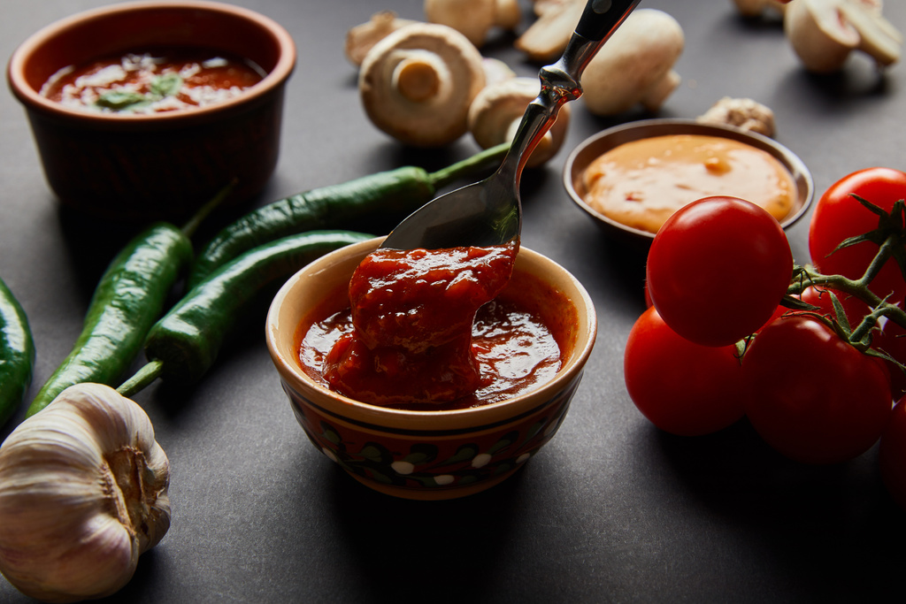 вибірковий фокус ложки в смачному томатному соусі поблизу стиглих овочів на чорному
 - Фото, зображення