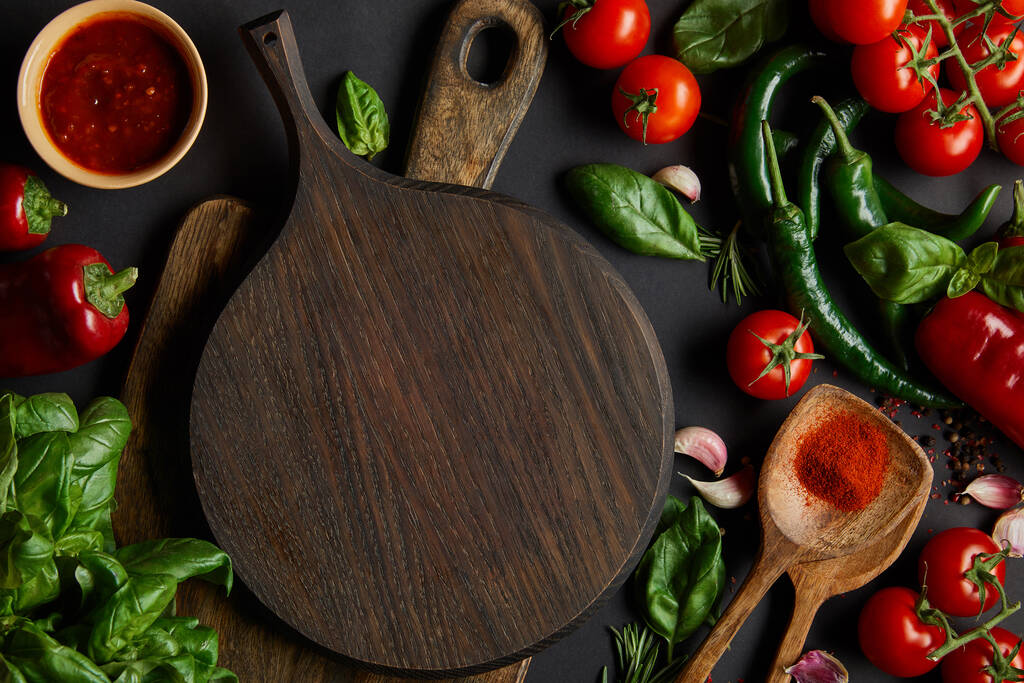 widok z góry czerwonych pomidorów wiśniowych, sos pomidorowy, papryka, zioła i zielona papryka chili w pobliżu cięcia desek na czarno - Zdjęcie, obraz