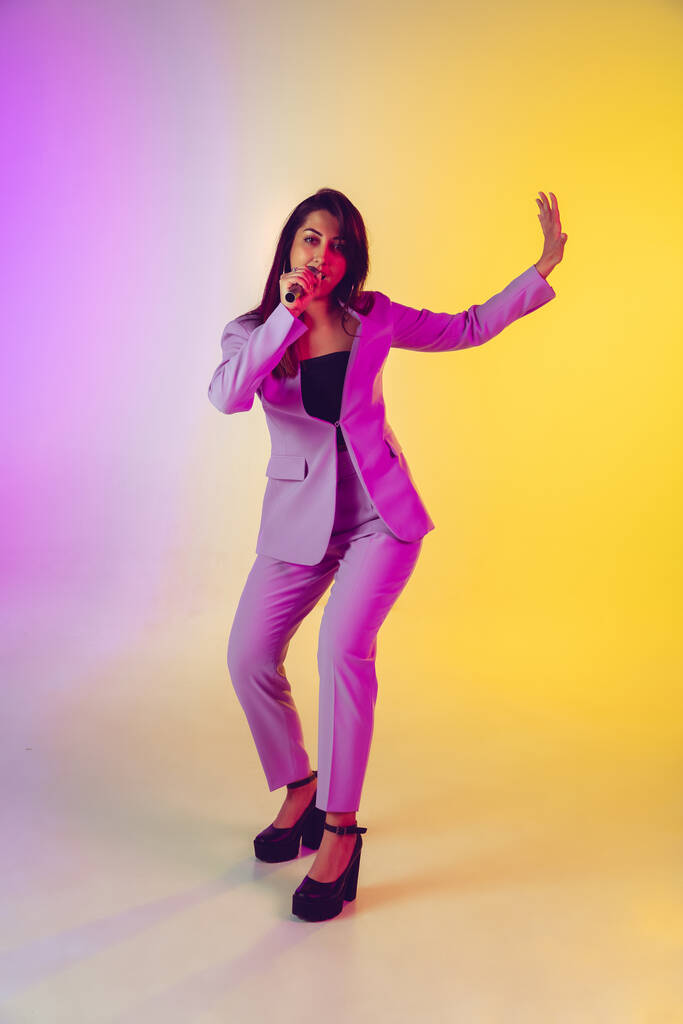 Caucasian female singer portrait isolated on gradient studio background in neon light - Photo, Image