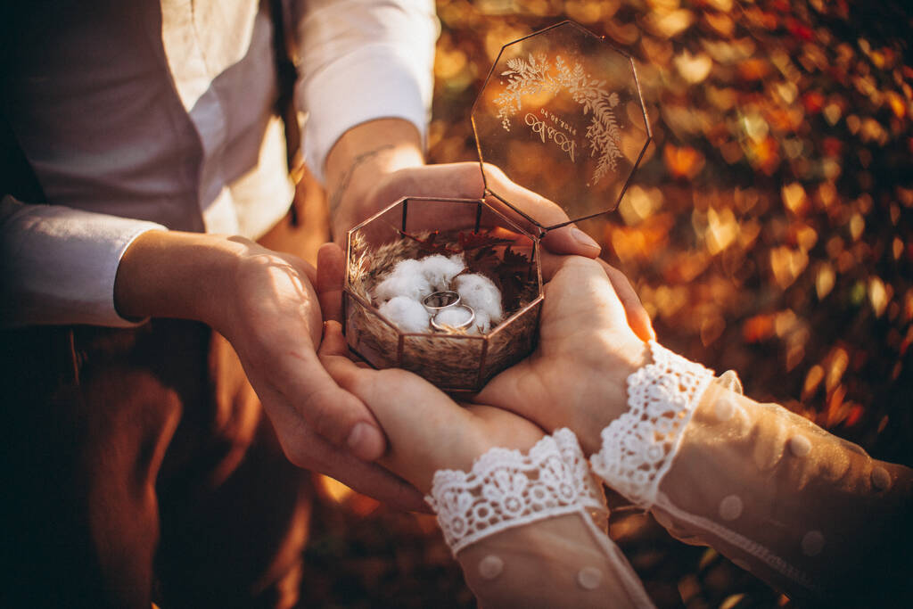 alianças de casamento em uma caixa de vidro elegante decorada com uma flor de algodão com um fundo natural borrado na forma de muitos corações brilhantes
 - Foto, Imagem