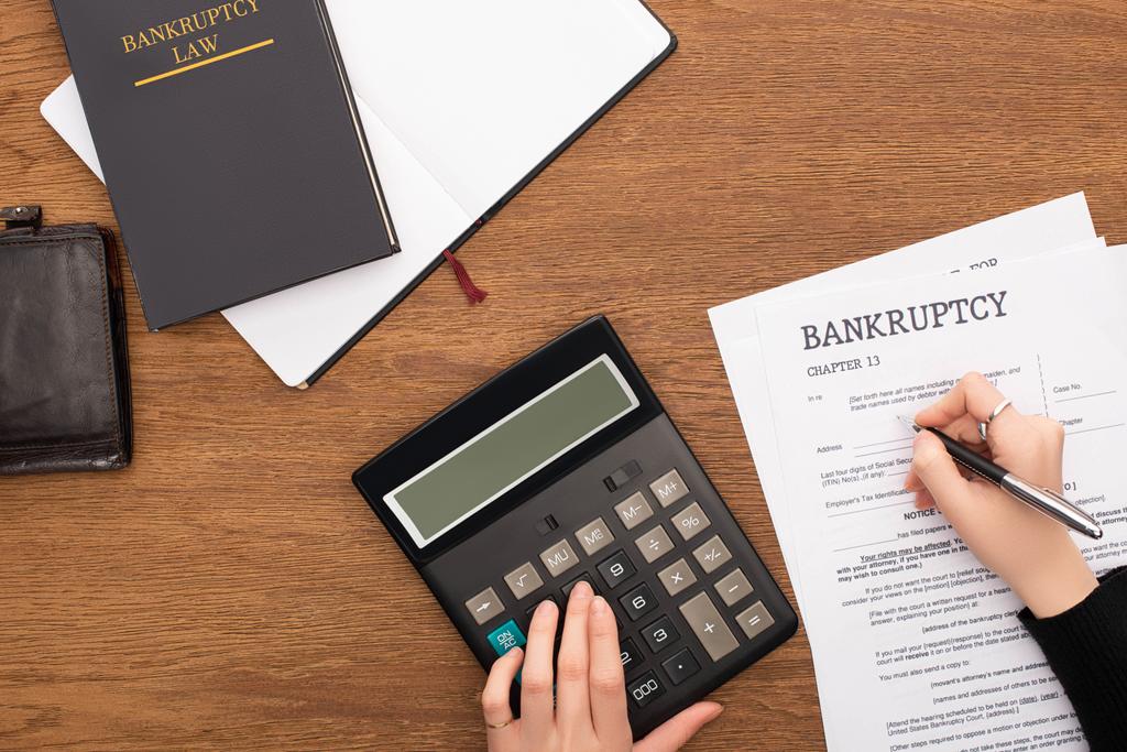 partial view of woman filling in bankruptcy form and using calculator on wooden background - Photo, Image