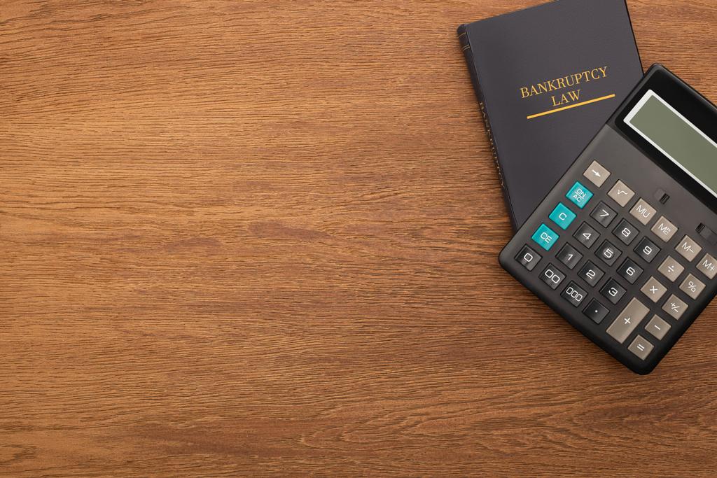 górny widok książki prawa upadłościowego i kalkulatora na drewnianym tle - Zdjęcie, obraz
