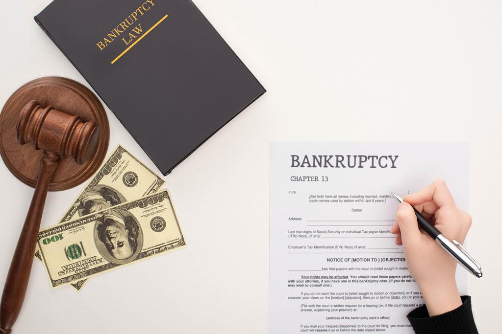 cropped view of woman filling in bankruptcy form with pen near money, gavel and bankruptcy law book on white background - Photo, Image