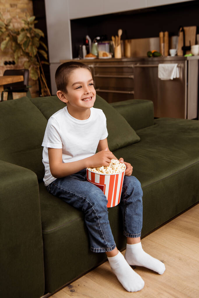 Весела дитина тримає відро з попкорном і дивиться телевізор вдома
  - Фото, зображення