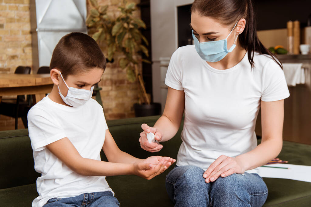 Matka a syn v lékařských maskách pomocí ruční dezinfekci doma  - Fotografie, Obrázek