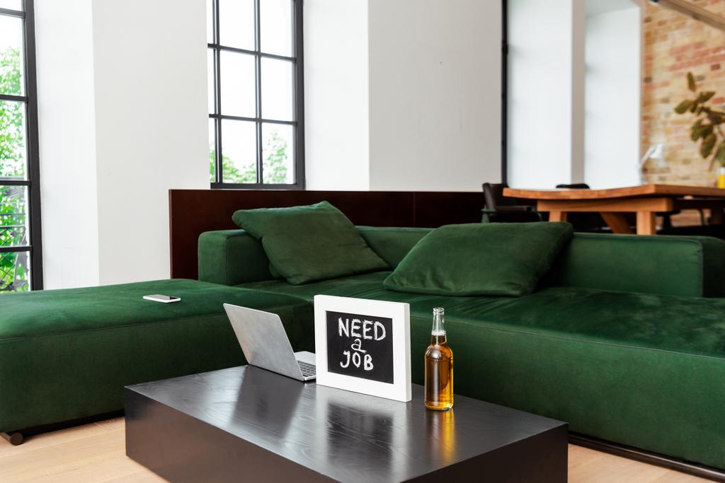 Laptop in der Nähe von Kreide mit Job-Schriftzug und Bierflasche in der Nähe von modernem Sofa - Foto, Bild