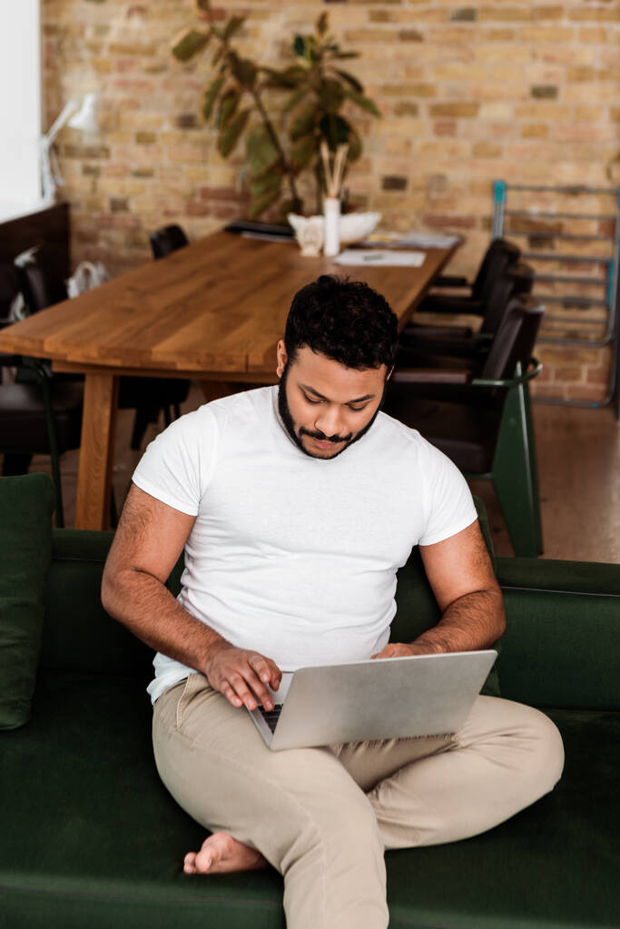 handsome african american freelancer using laptop in living room  - Photo, Image