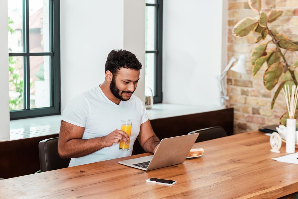 bearded african american freelancer working from home and holding glass of orange juice  - Photo, Image