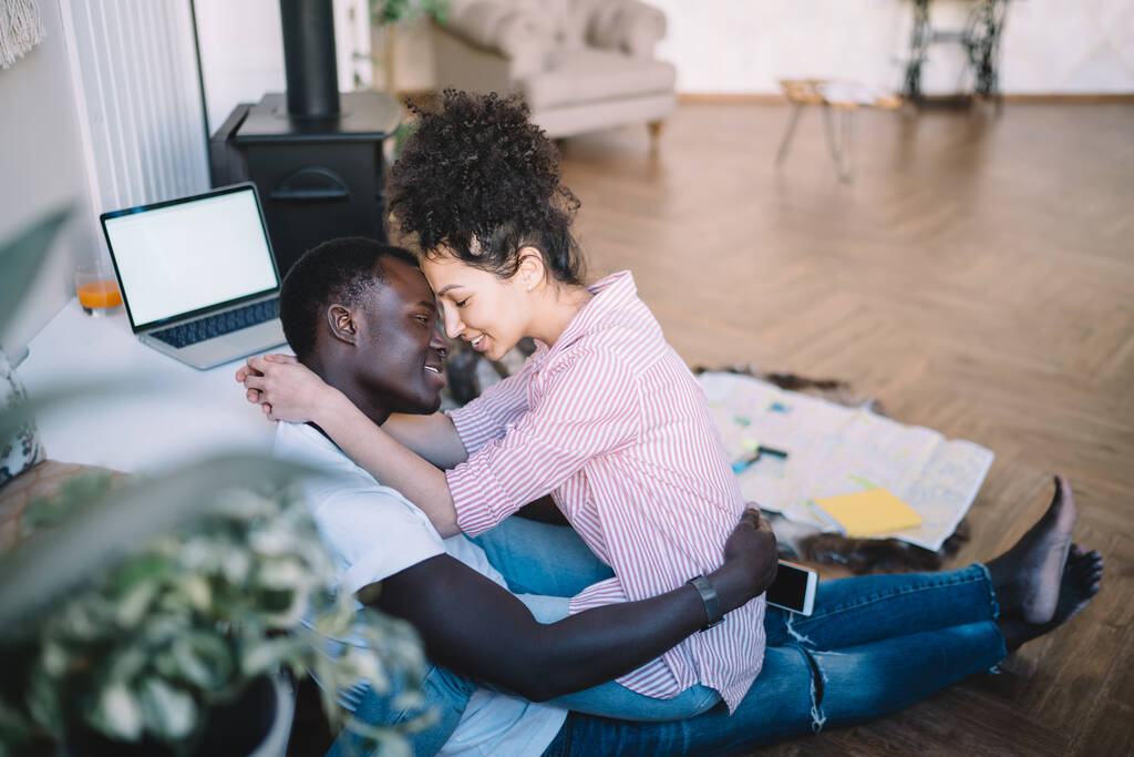 Afro-Américain en t-shirt blanc et jeans avec montre-bracelet et smartphone embrassant femme ethnique avec les cheveux sales dans des vêtements décontractés - Photo, image