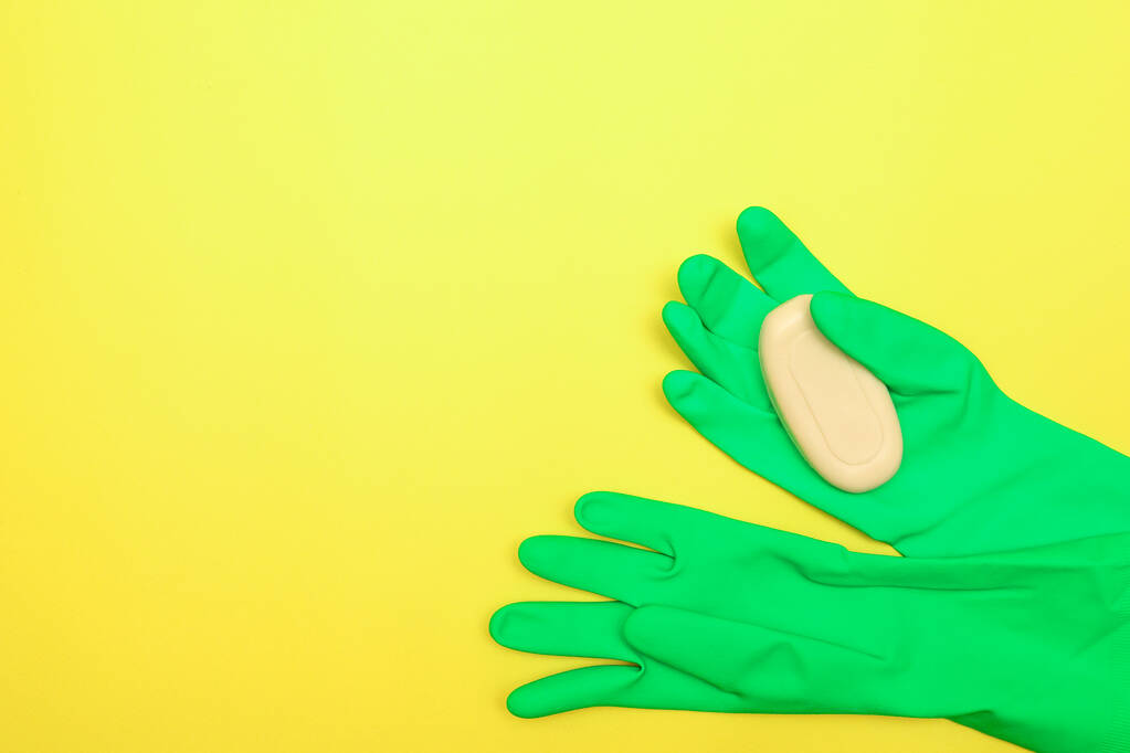 Het begrip reinheid en hygiëne. Zeep in rubberen handschoenen op een gele achtergrond. Desinfectie. Ruimte voor tekst, platte lay. - Foto, afbeelding