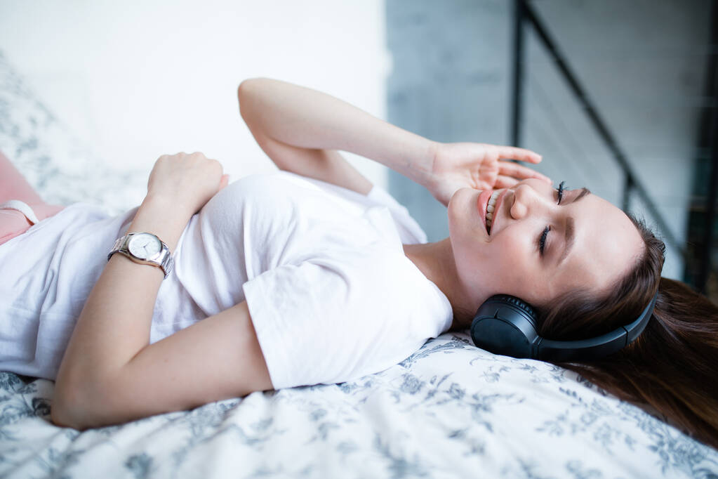 Atraktivní student poslouchá ráno na posteli hudbu na sluchátkách. Koncept volného času a rekreace - Fotografie, Obrázek