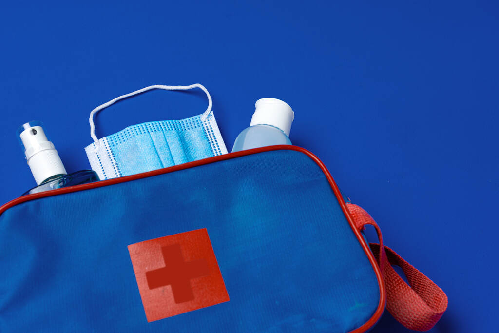 Verbandskasten mit Maske und Desinfektionsmittel auf blauem Hintergrund - Foto, Bild