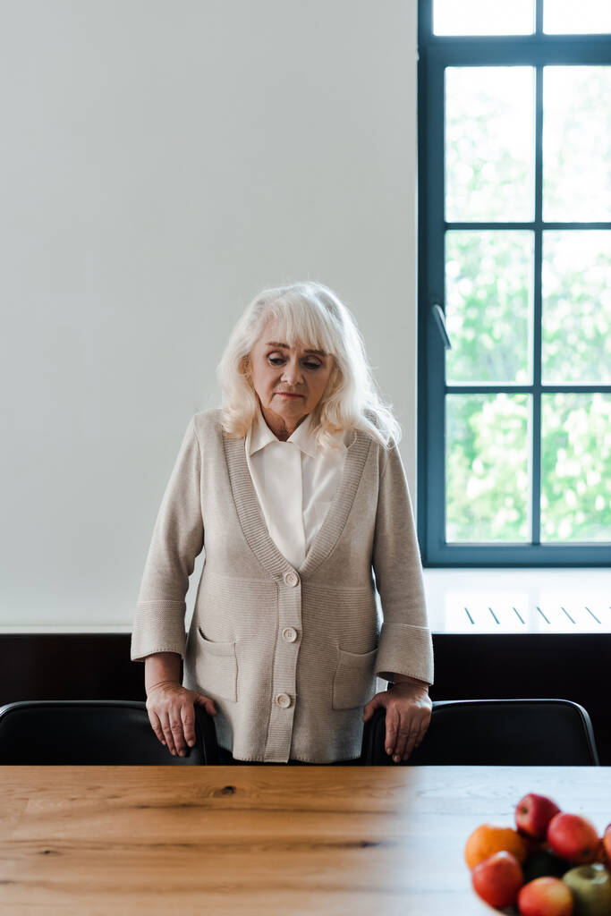 sconvolto donna anziana solitaria in piedi a tavola con frutta durante la quarantena
 - Foto, immagini