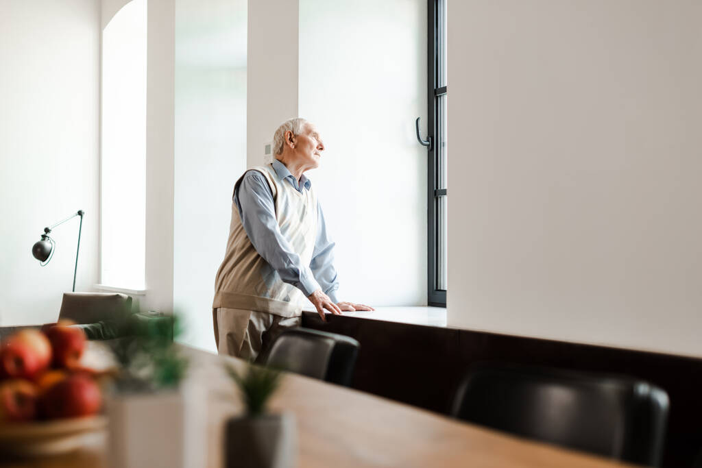 Verärgerter älterer Mann, der während der Quarantäne am Fenster steht, selektiver Fokus - Foto, Bild