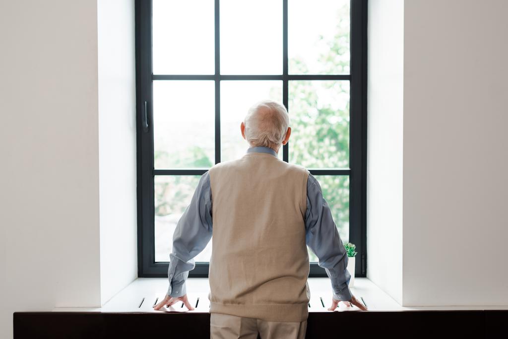 vista trasera del anciano solitario de pie cerca de la ventana durante la cuarentena
 - Foto, imagen