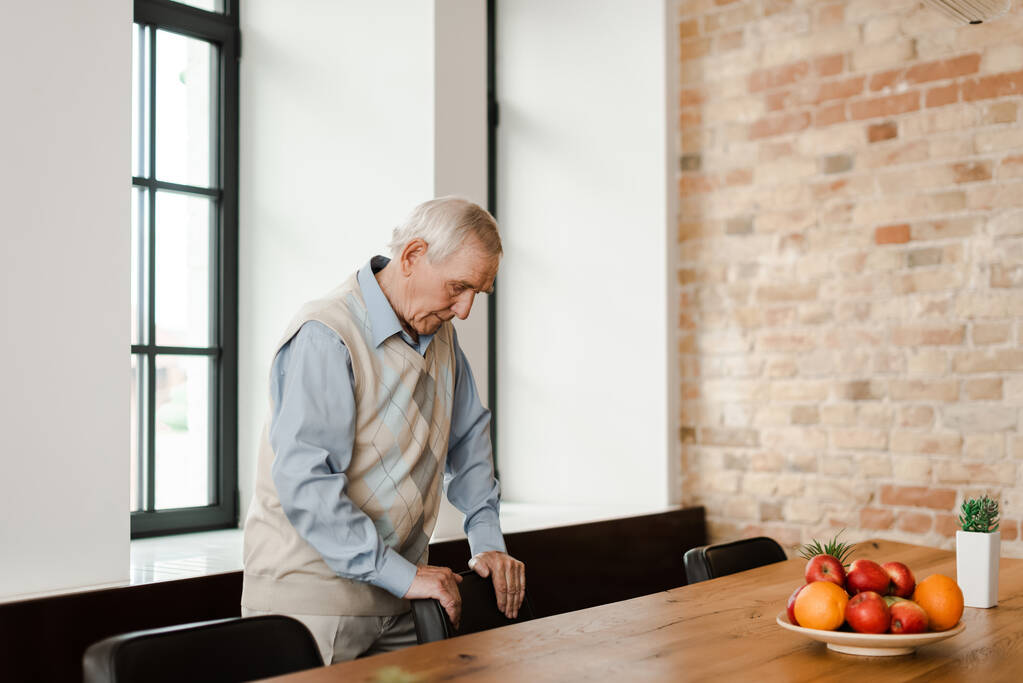 засмучений літній чоловік стоїть за столом з фруктами під час карантину
  - Фото, зображення