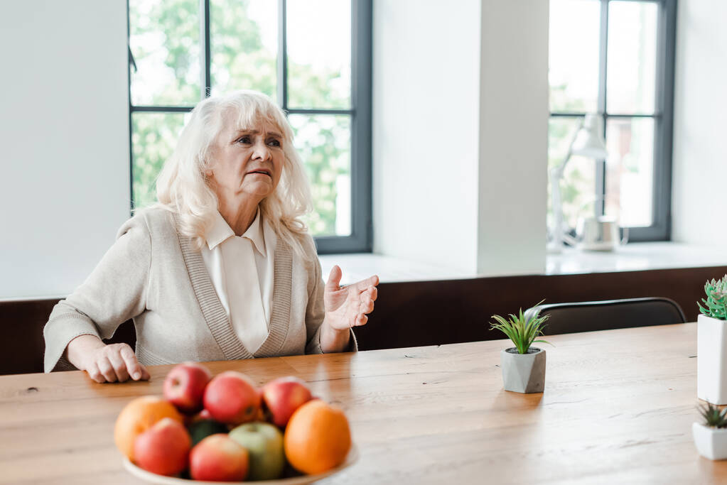беспокойная пожилая женщина сидит за столом с фруктами во время самоизоляции
 - Фото, изображение