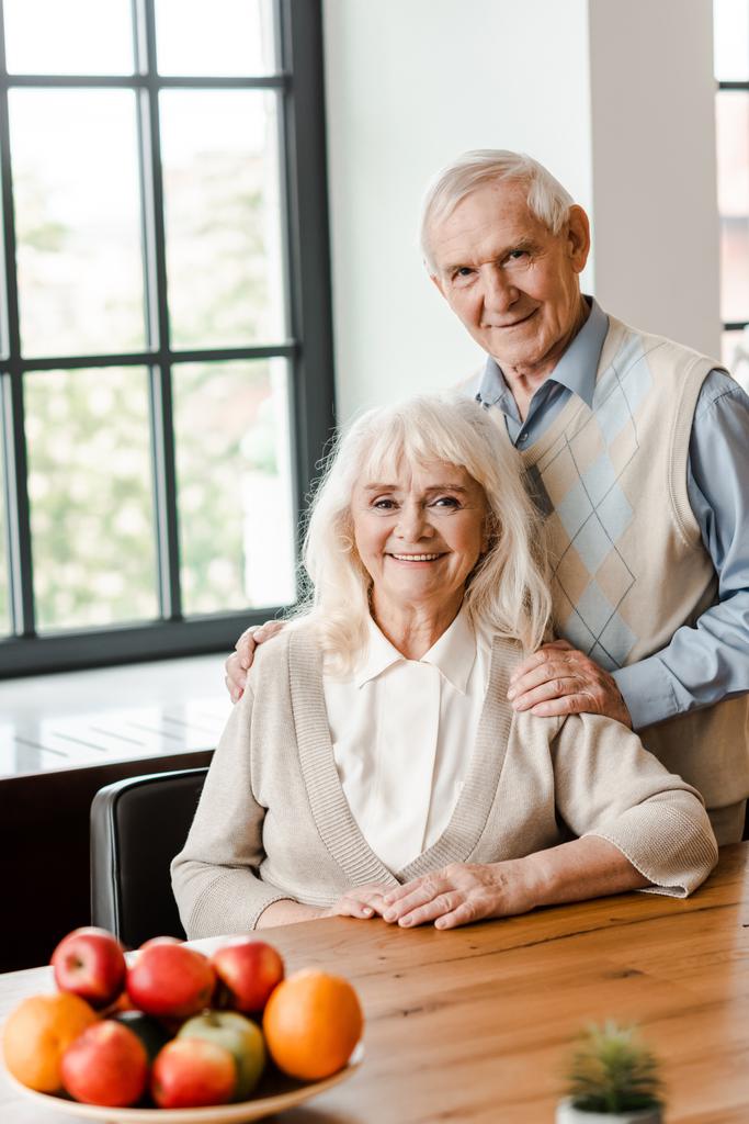 χαμογελαστό ηλικιωμένο ζευγάρι κάθεται στο τραπέζι με φρούτα  - Φωτογραφία, εικόνα