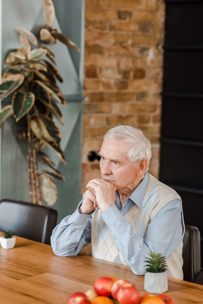 figyelmes idős ember gyümölcsökkel és növényekkel az asztalon az önelkülönítés során  - Fotó, kép