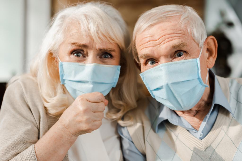 эмоциональная пожилая пара в медицинских масках, показывающая кулак во время самоизоляции
 - Фото, изображение