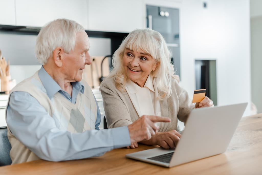 felice coppia di anziani shopping online con carta di credito e puntando al computer portatile a casa durante l'isolamento
 - Foto, immagini