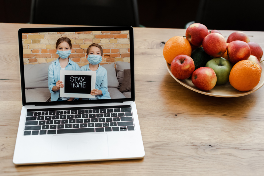 közeli-ból laptop-val testvérek-ban orvosi maszkok gazdaság otthon jel az asztalon gyümölcsökkel  - Fotó, kép