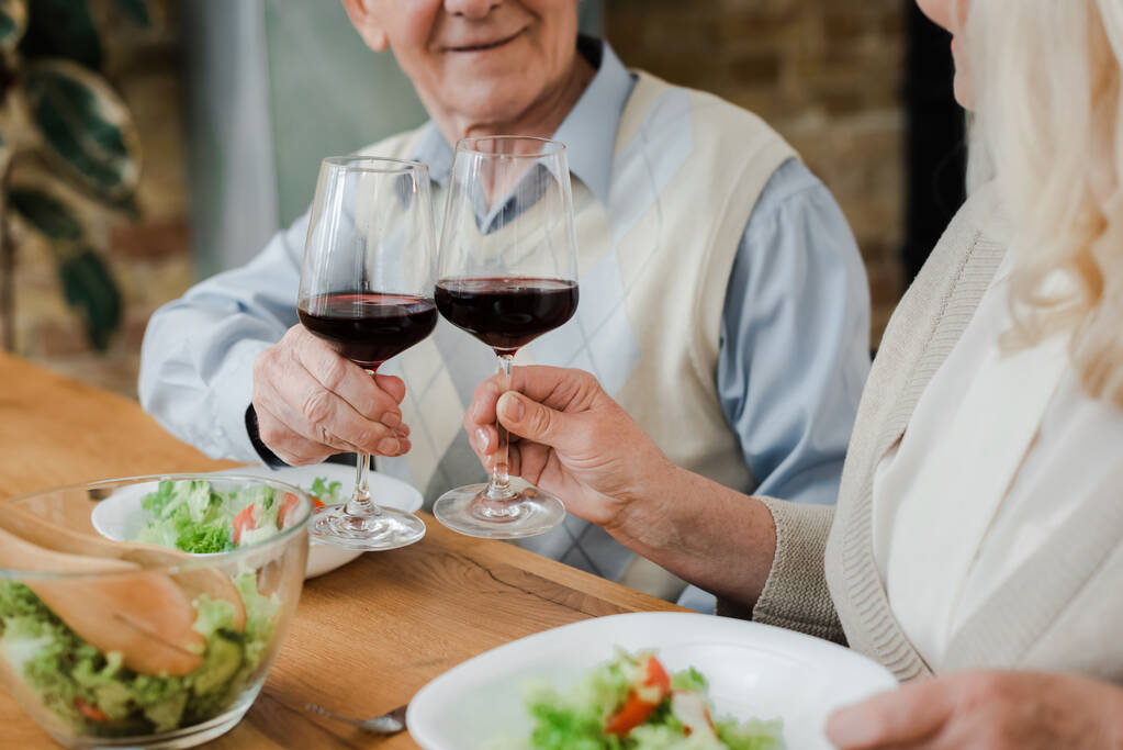cropped view of elderly couple having dinner with wine and salad at home on self isolation - Photo, Image