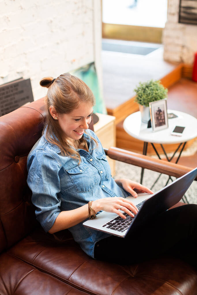 Femme souriante qui se refroidit avec un ordinateur portable dans un café. Contenu femme occasionnelle assis sur un canapé confortable et en utilisant un ordinateur portable heureux
 - Photo, image