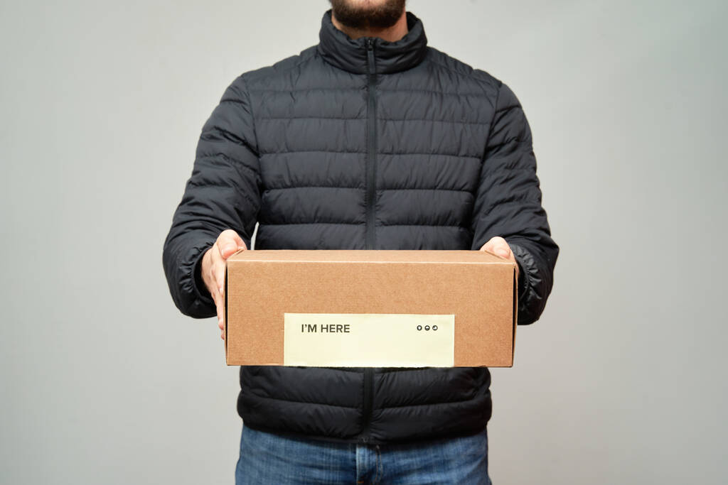 Le courrier tient une boîte devant lui avec les mots "Je suis ici" sur un fond blanc isolé. Service de livraison
. - Photo, image