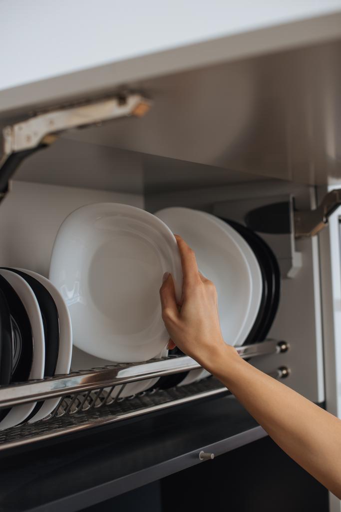 oříznutý pohled na hospodyňku, jak umisťuje čistý talíř na stojan v kuchyni - Fotografie, Obrázek