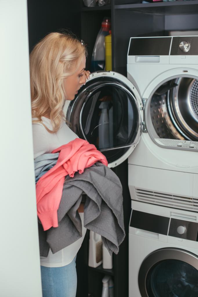 молодая блондинка домохозяйка с прачечной рядом с открытой стиральной машиной
 - Фото, изображение