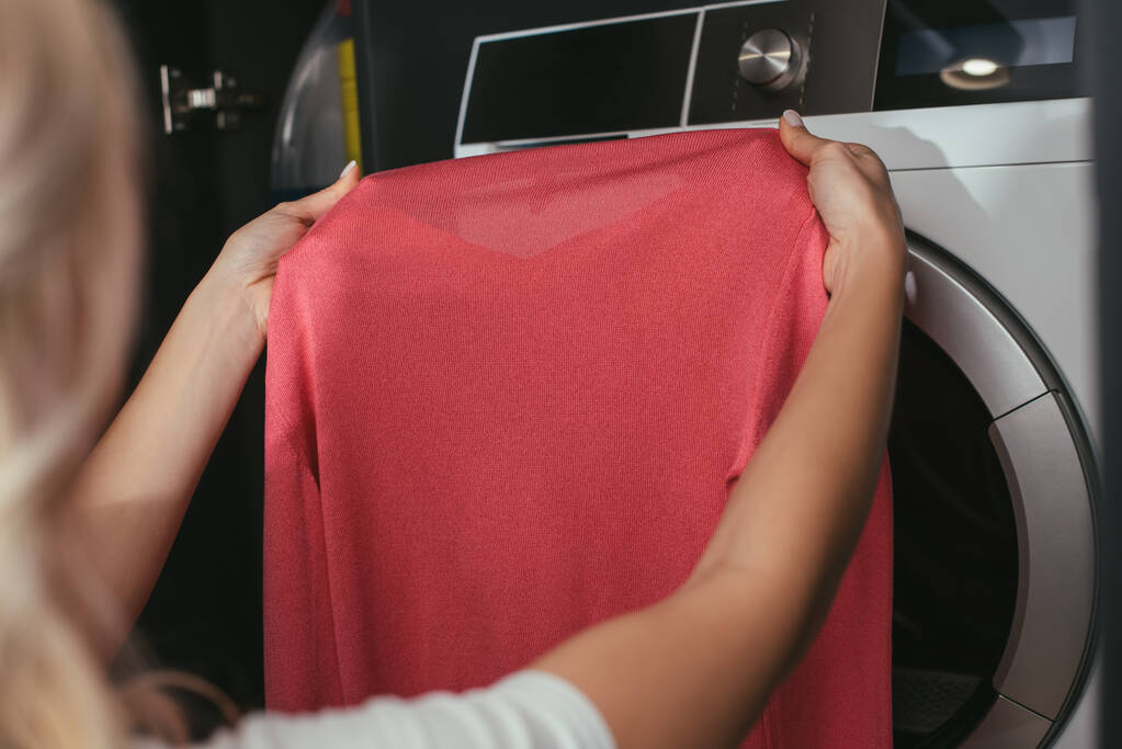 vista cortada de dona de casa segurando pulôver perto da máquina de lavar roupa
 - Foto, Imagem