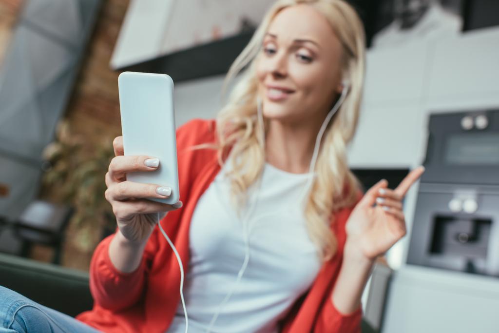 selektywne skupienie kobiety w słuchawkach pokazujące gest idei patrząc na smartfona - Zdjęcie, obraz