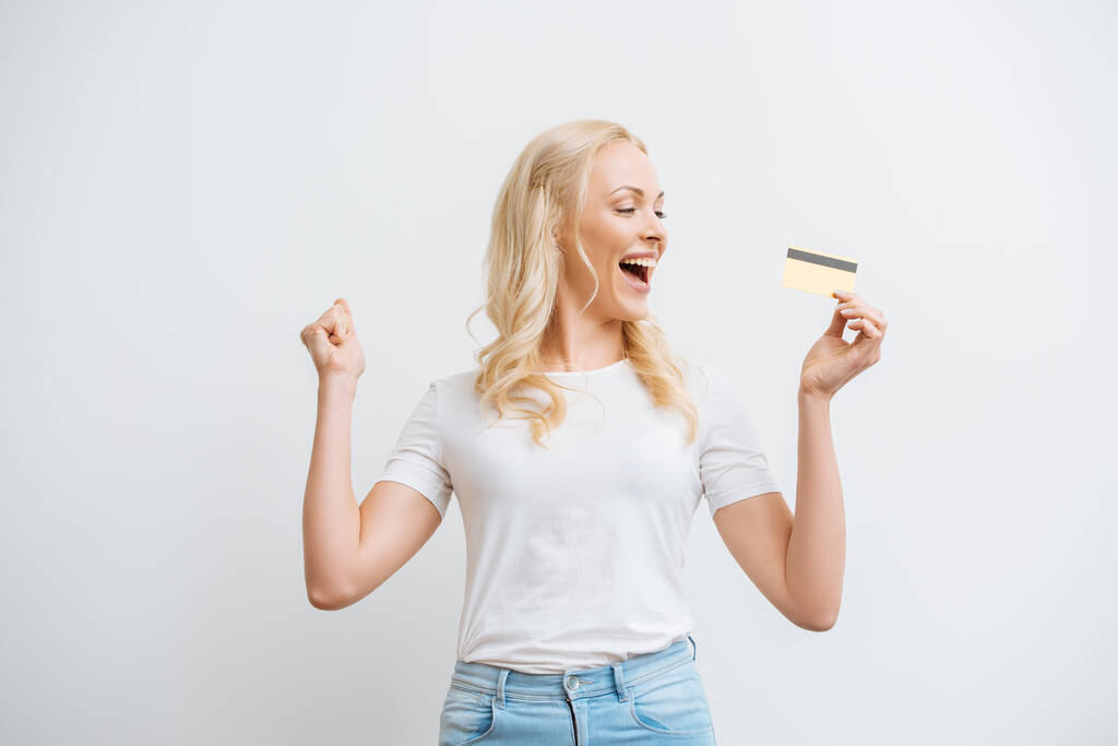szczęśliwa kobieta pokazując gest zwycięzca trzymając kartę kredytową izolowane na białym - Zdjęcie, obraz