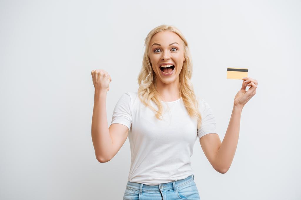 excited woman showing winner gesture while holding credit card isolated on white - Photo, Image