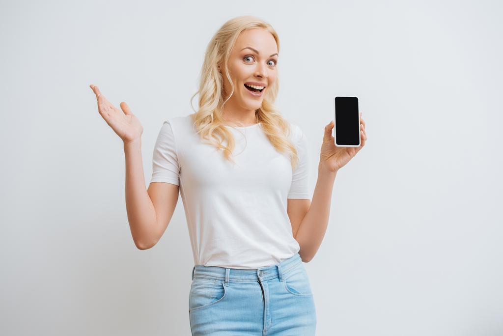 excited woman showing smartphone with blank screen while looking at camera isolated on white - Photo, Image