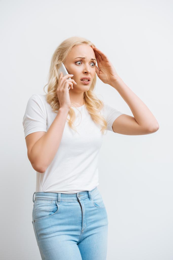 σοκαρισμένη γυναίκα αγγίζοντας το κεφάλι, ενώ μιλάμε για smartphone απομονώνονται σε λευκό - Φωτογραφία, εικόνα