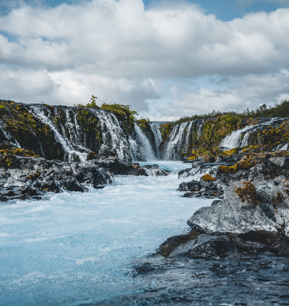 Dramatic views of the bright powerful Bruarfoss bluw waterfall. Popular tourist attraction. Blue sky and clouds during midnight sun. Location place Brekkuskogur South Iceland, Europe. - Photo, Image