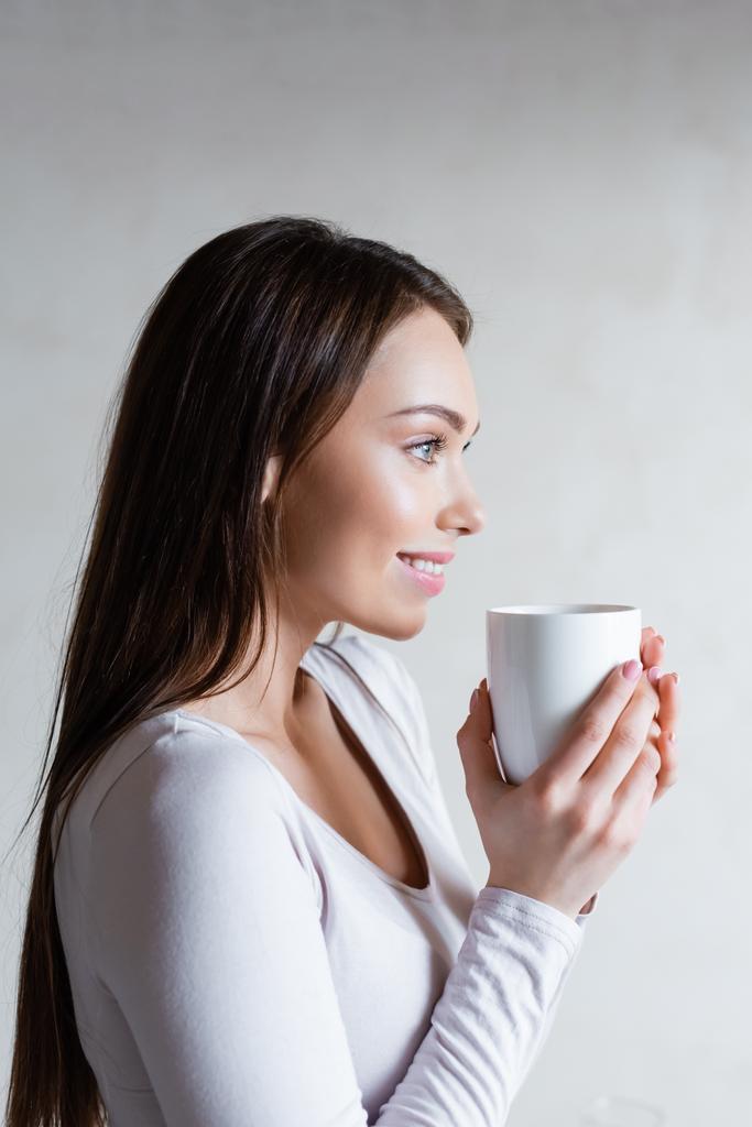 vue latérale de la femme gaie tenant une tasse de thé et souriant à la maison
  - Photo, image