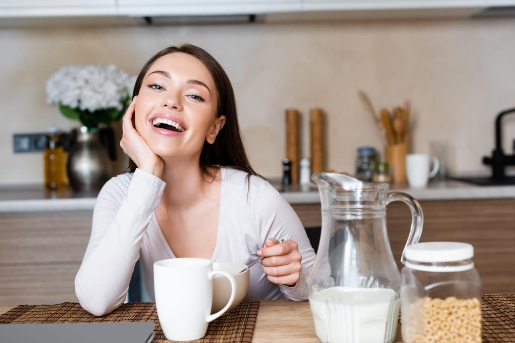 счастливая девушка держит ложку возле миски, чашку и кувшин с молоком
  - Фото, изображение