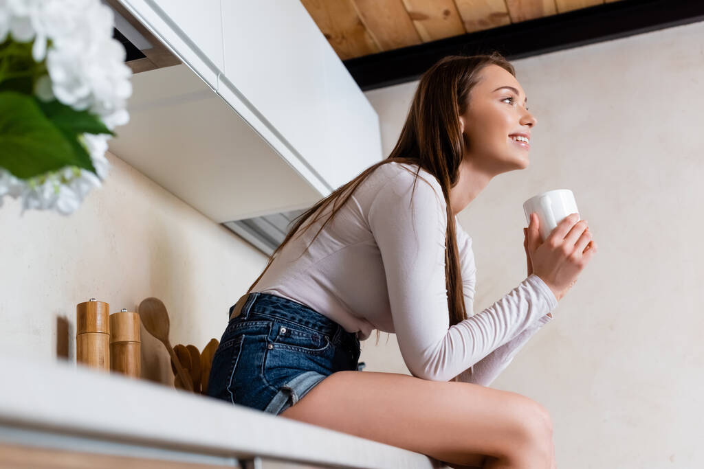 вибірковий фокус усміхненої дівчини, що сидить і тримає чашку кави
 - Фото, зображення