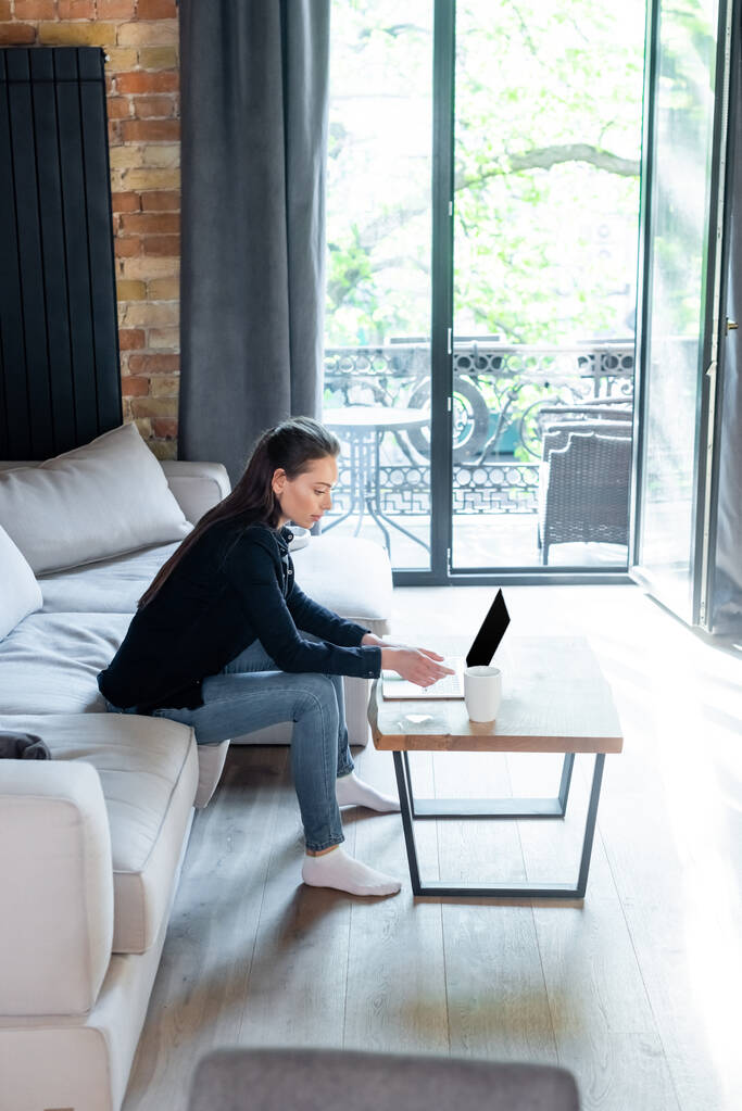 Freelancer atraente usando laptop com tela em branco perto da xícara de café na mesa de café
  - Foto, Imagem