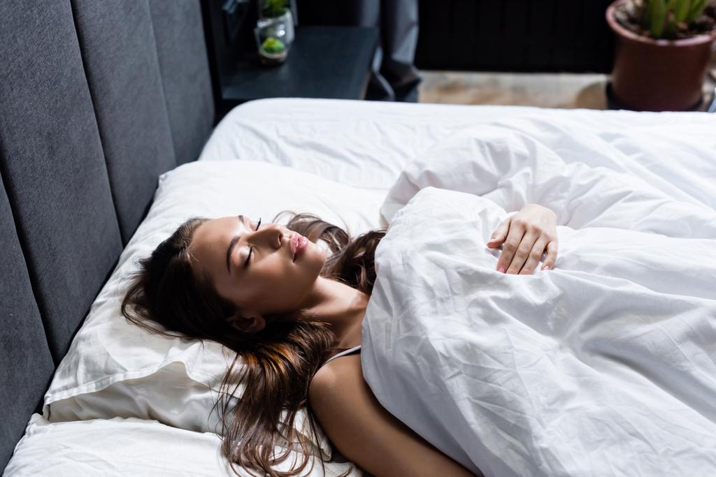 młoda kobieta śpi w łóżku pod kocem  - Zdjęcie, obraz